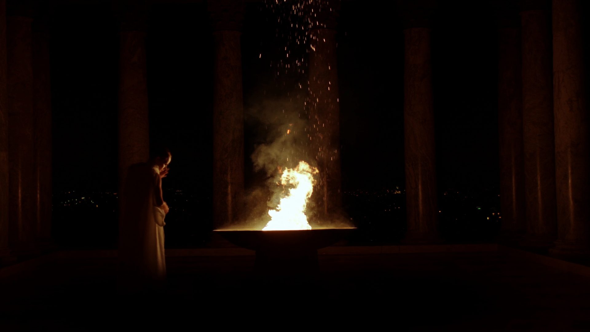 A lone Vestal tends the eternal flame in a dark Roman temple